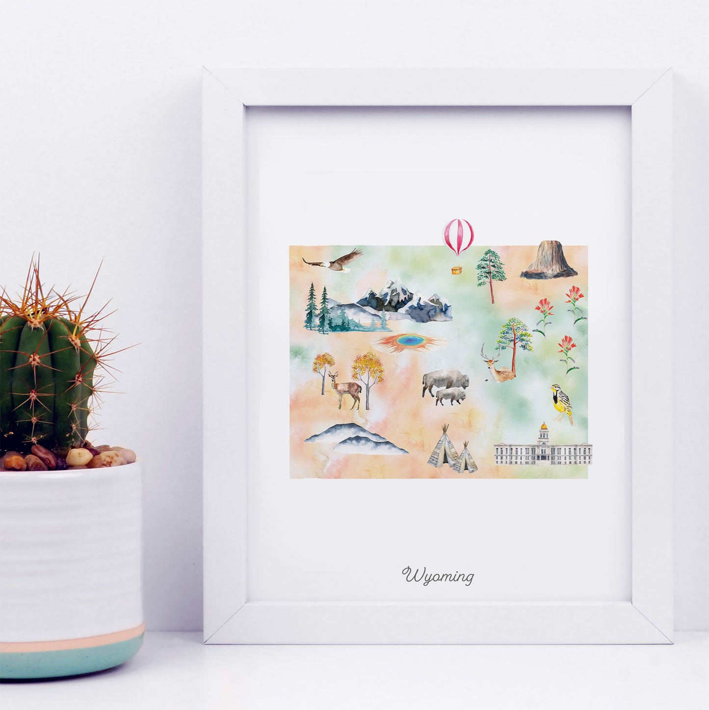A framed watercolor illustration depicting various scenes and landmarks associated with Wyoming, including mountains, wildlife, and buildings.