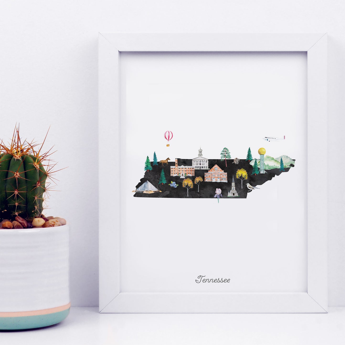 A framed illustration of Tennessee's state map, featuring various landmarks and symbols, is displayed next to a potted cactus plant.