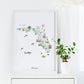a framed watercolor map of Florida, with various landmarks and symbols representing different aspects of the state. The map is displayed on a white shelf, and there is a potted plant next to it.