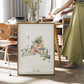 A framed watercolor illustration of New York is displayed on a table, with a person standing next to it.