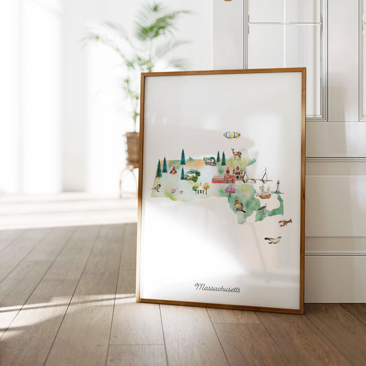 A framed illustration of a map of Massachusetts, featuring various landmarks and symbols, is displayed on a wooden floor against a white wall.