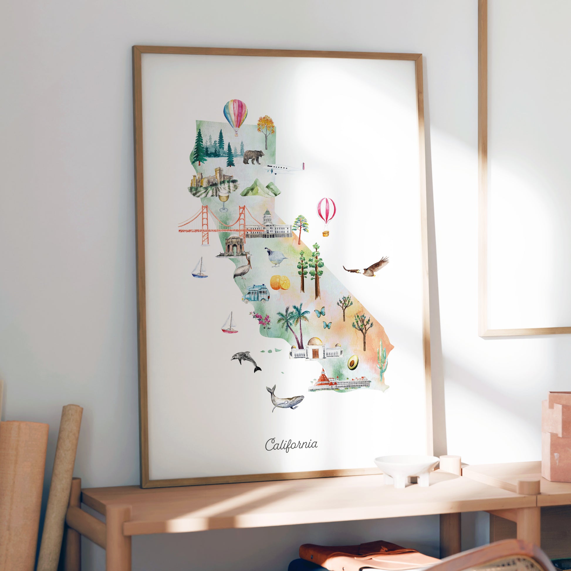 The image is a framed poster of a colorful illustration depicting various landmarks and scenes from California, including the Golden Gate Bridge, palm trees, hot air balloons, and other iconic symbols.