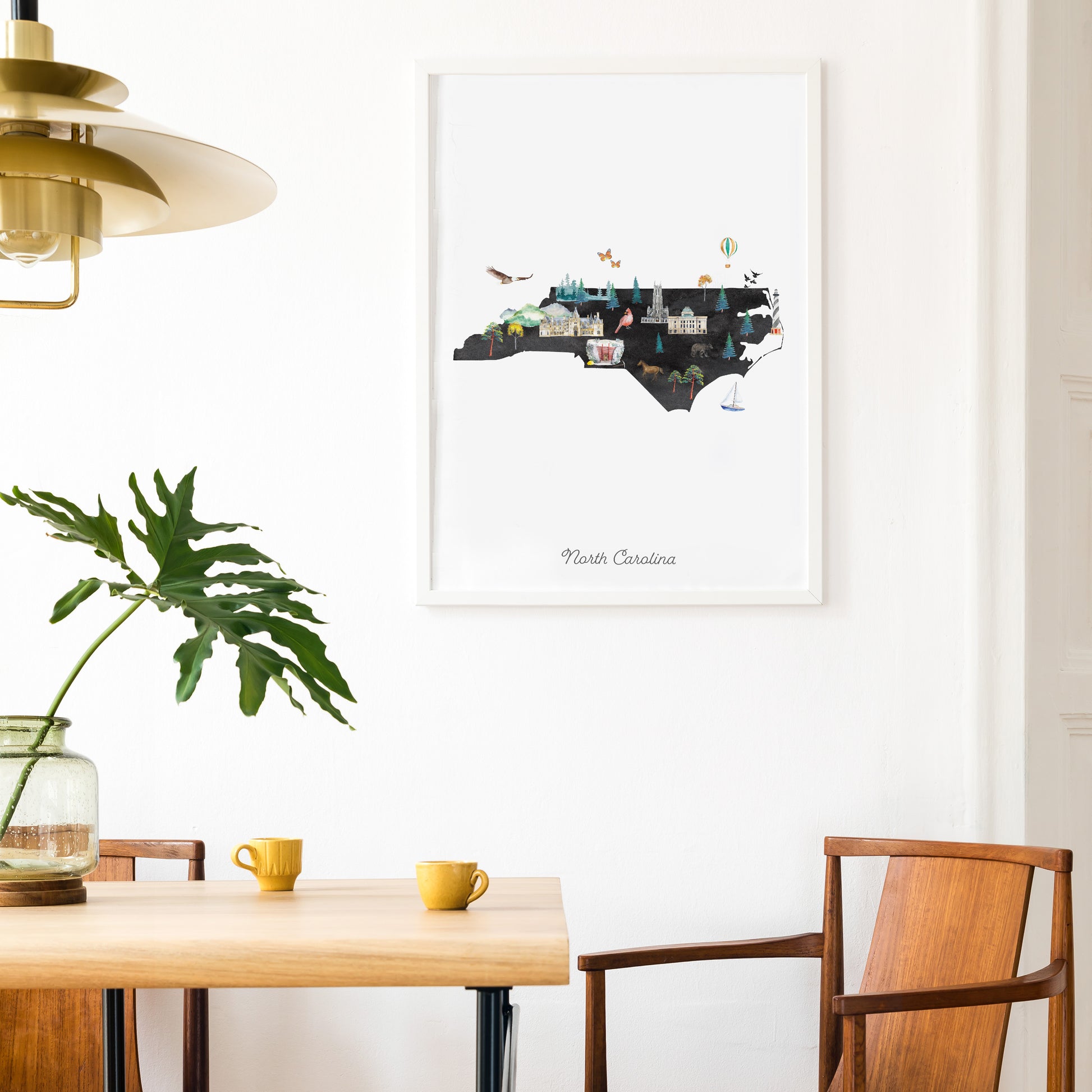a dining area with a wooden table, two yellow mugs, and a framed print of a map of North Carolina hanging on the wall.
