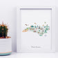 A framed watercolor illustration depicting various landmarks and scenes from North Carolina, including a cactus, a bird, a hot air balloon, and a horse.