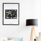 a framed artwork depicting various scenes and objects, including mountains, a hot air balloon, and a bird, hanging on a wall above a wooden floor lamp.