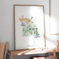 a framed watercolor painting of a map of Missouri, with various landmarks and symbols depicted.