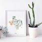 a framed watercolor illustration of the state of Texas, with various landmarks and icons representing different aspects of the state. The illustration is displayed next to a white vase with a potted cactus plant, creating a visually appealing and decorative arrangement.