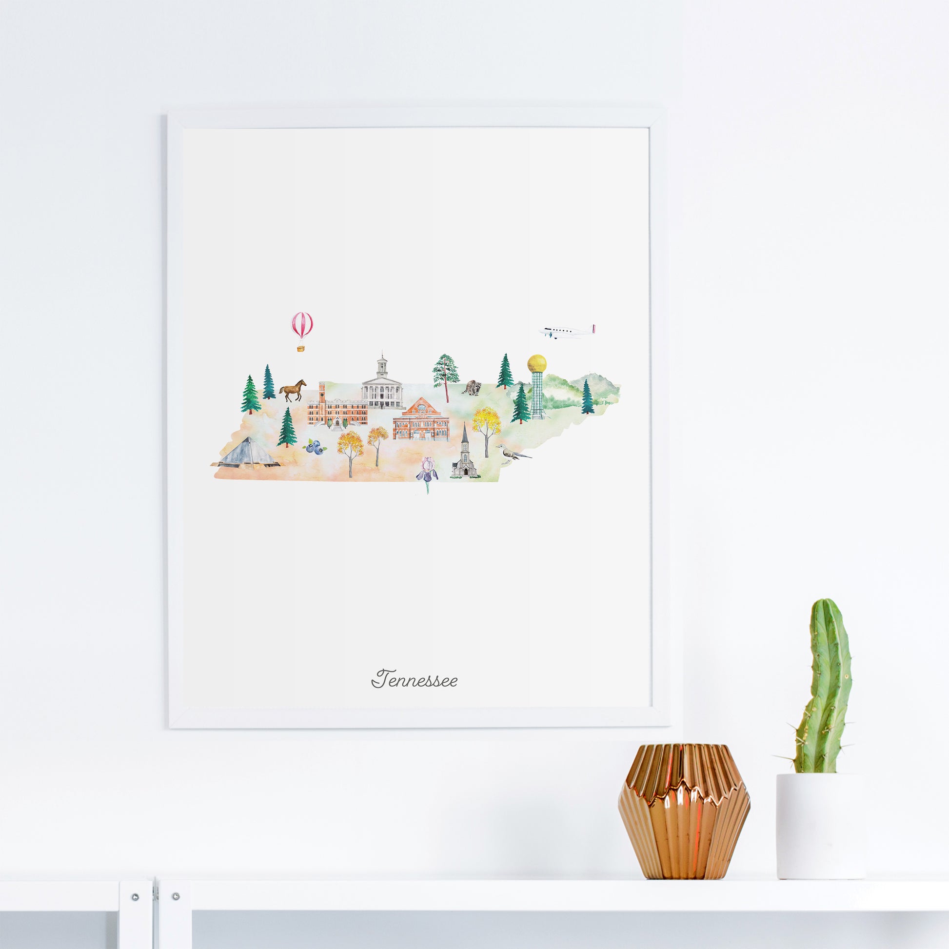 a framed watercolor illustration of a town in Tennessee, with various buildings, trees, and a hot air balloon in the background.