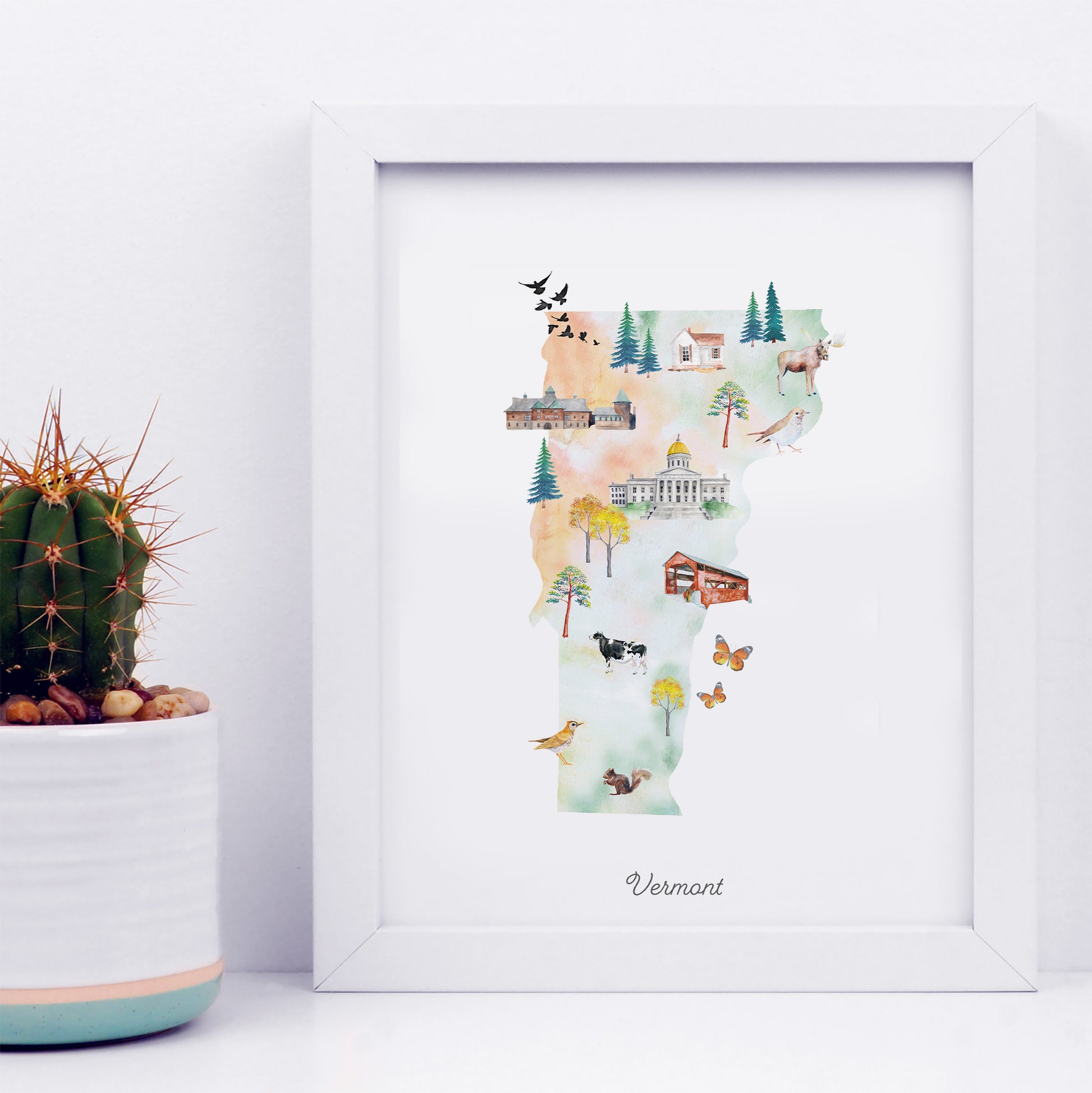 a framed watercolor illustration of the state of Vermont, depicting various landmarks and scenes from the state.