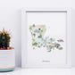 A framed watercolor illustration depicting various landmarks and scenes from Louisiana, including a cactus, a deer, a building, and a boat.