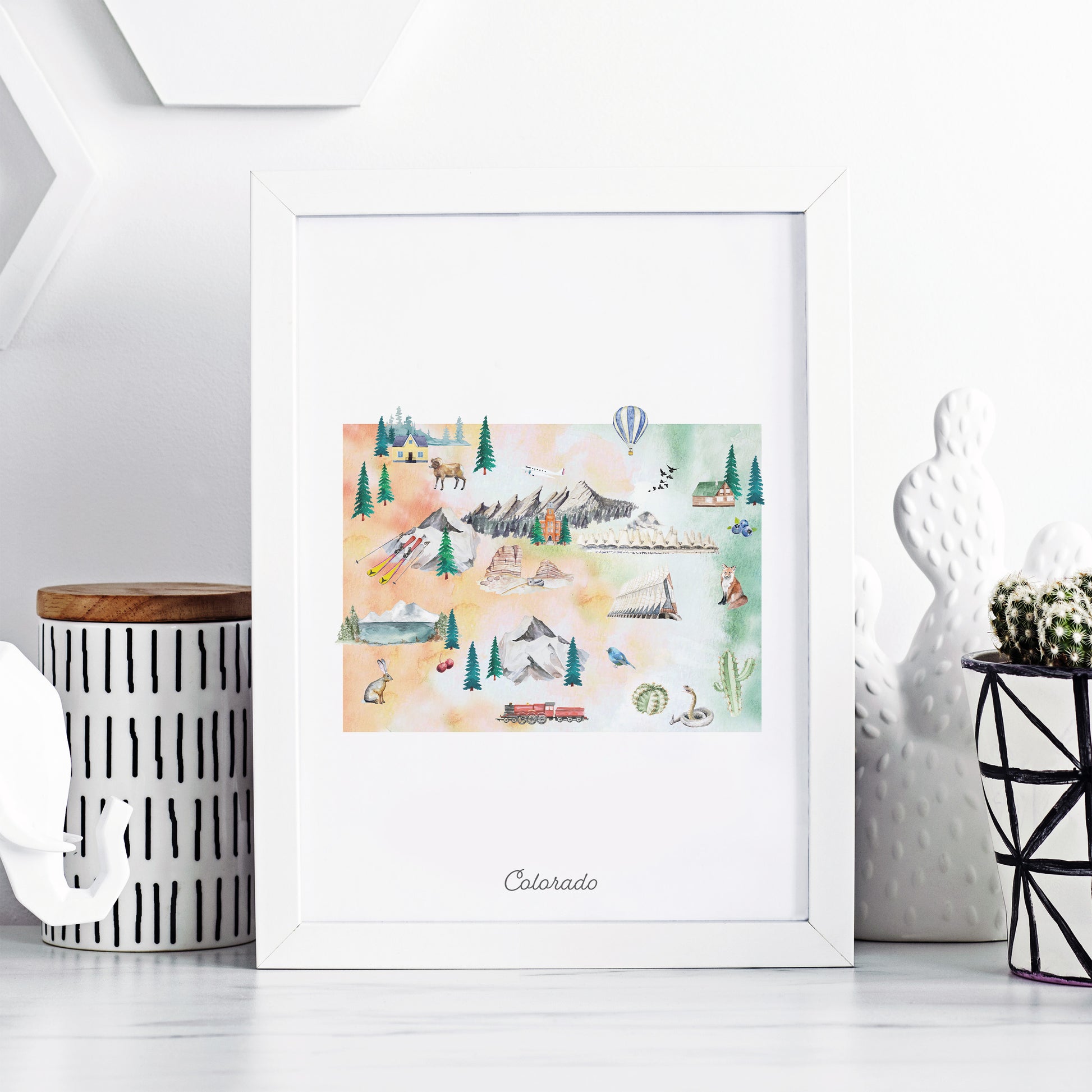 A framed watercolor painting depicting various scenes and landmarks of Colorado, including mountains, forests, and buildings, is displayed on a white shelf.
