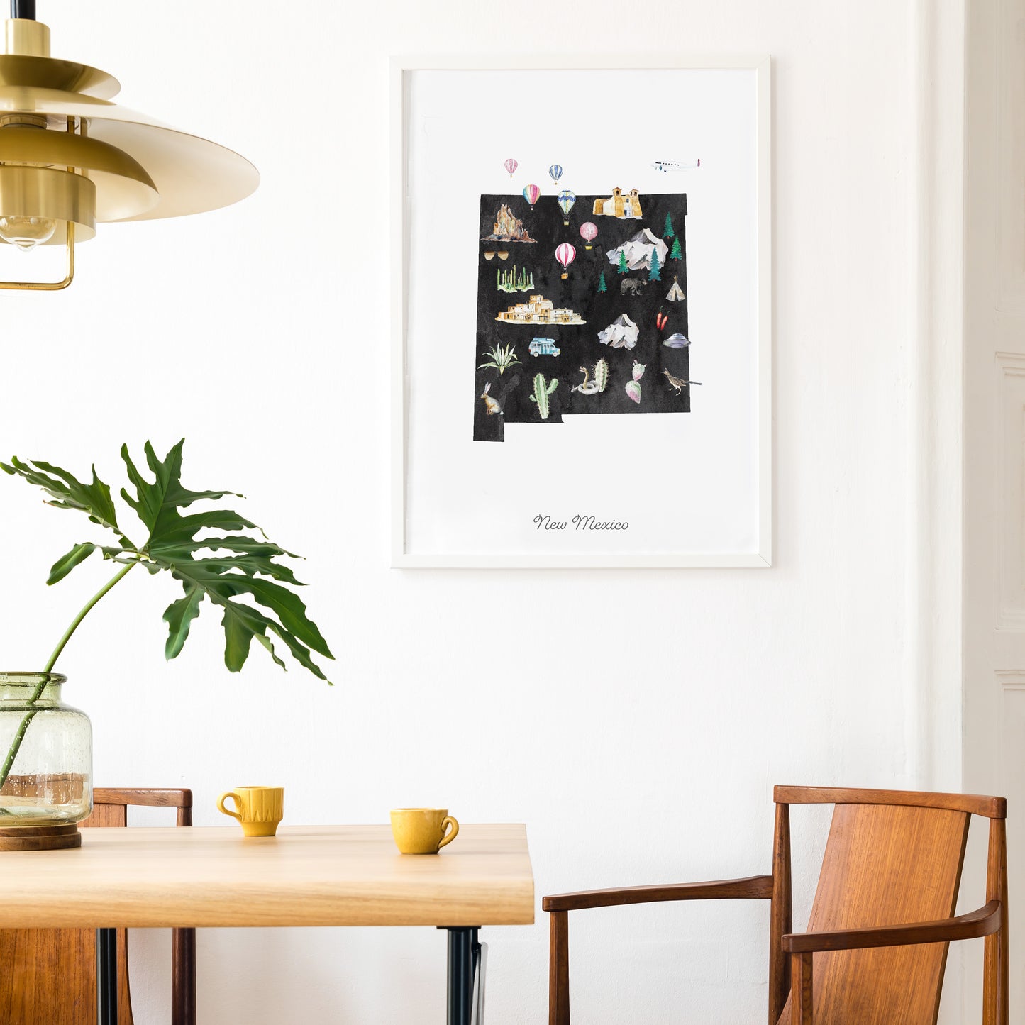 a dining area with a wooden table, two yellow mugs, and a framed poster of New Mexico hanging on the wall.