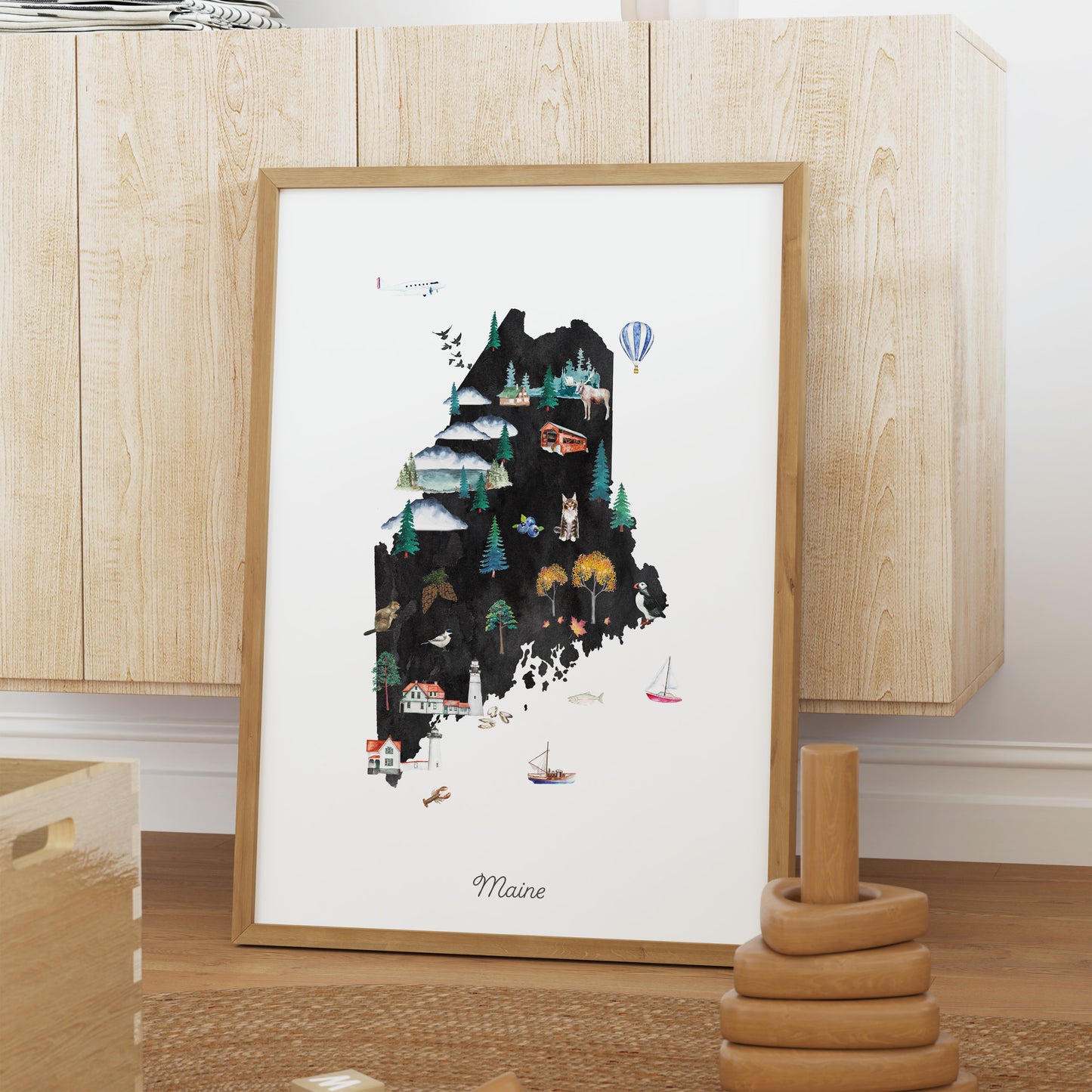 A framed illustration of the state of Maine, featuring various landmarks and scenes typical of the region.