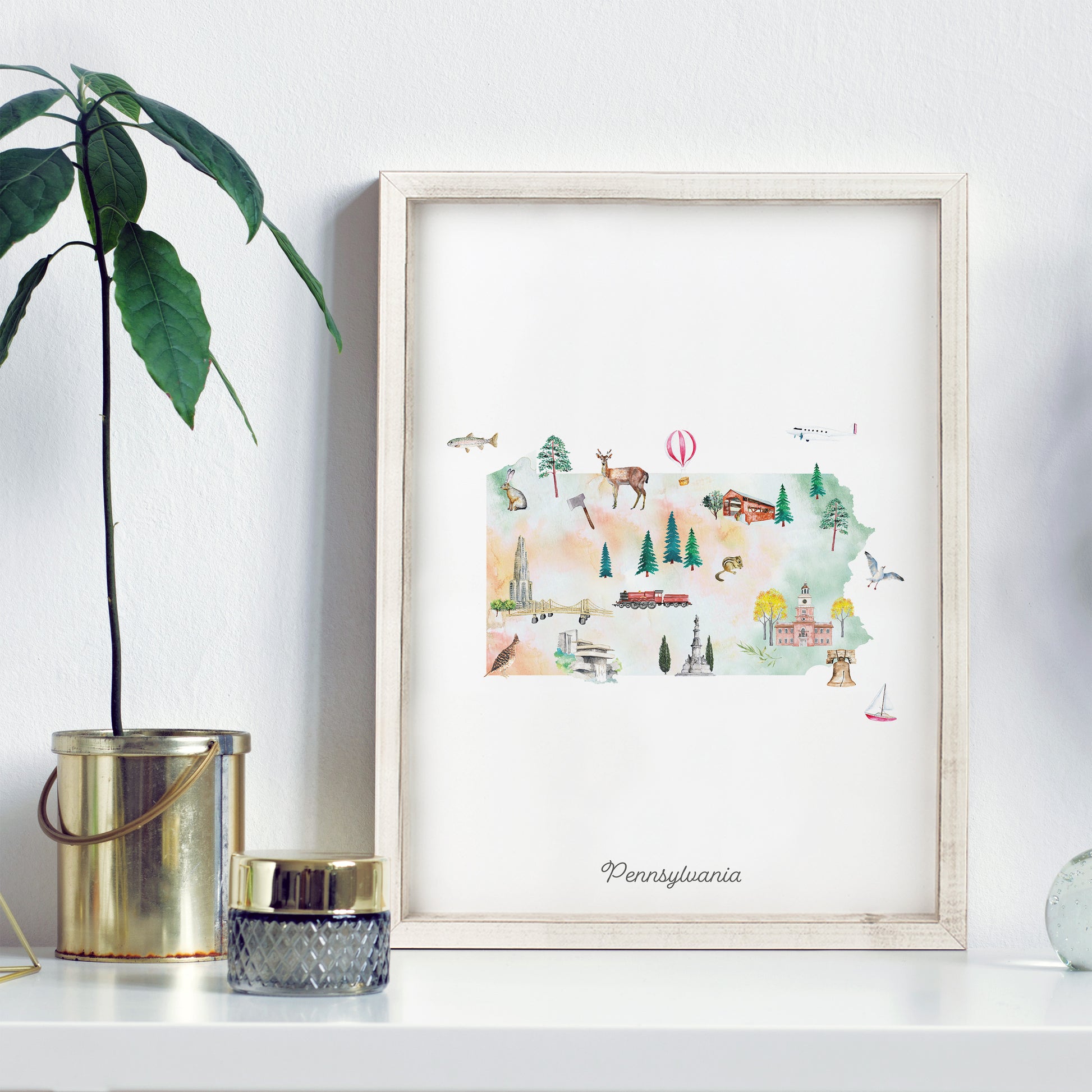 a framed watercolor illustration of Pennsylvania, with various landmarks and scenes depicted, such as a hot air balloon, a train, and a deer.