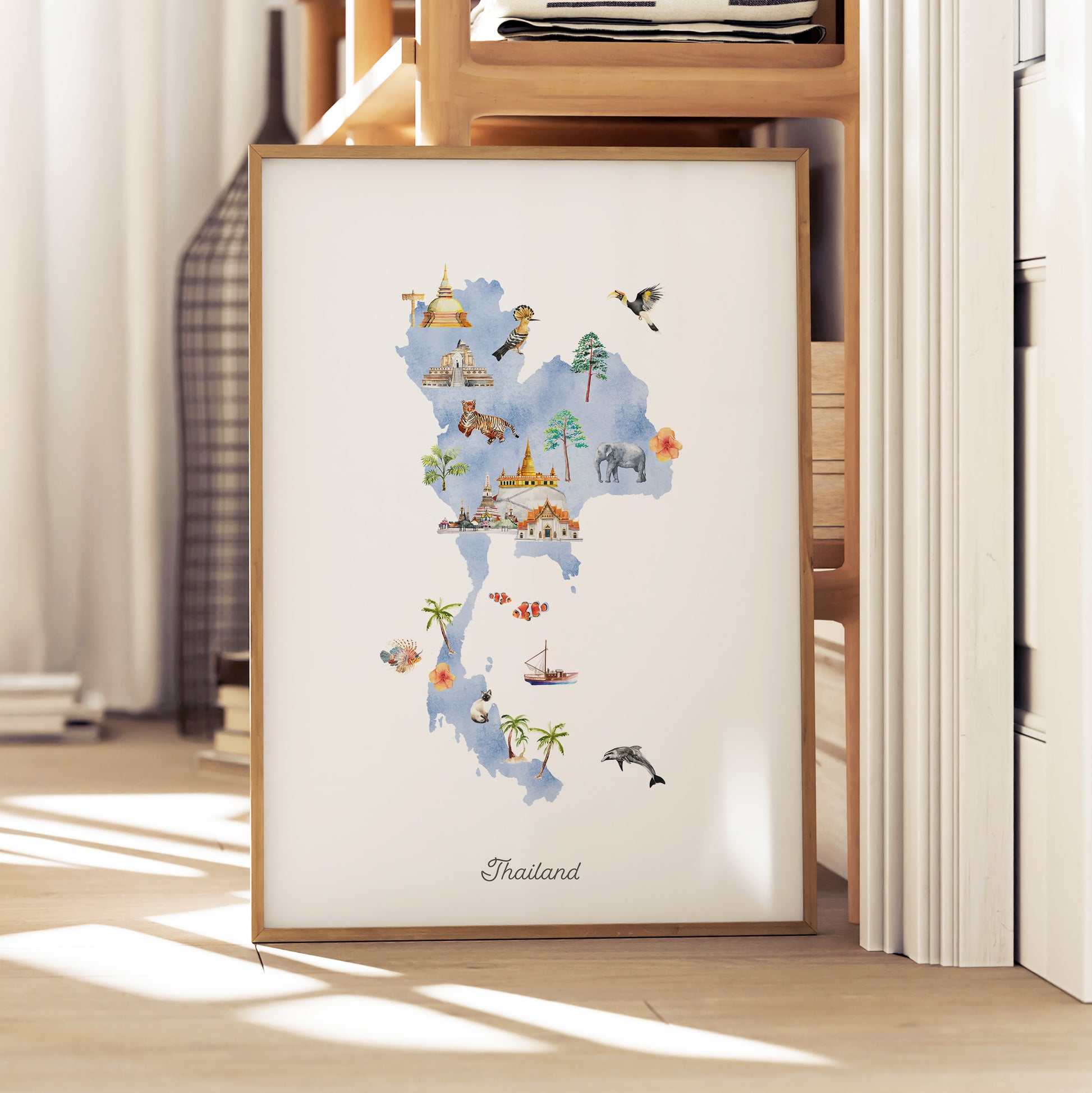A framed watercolor map of Thailand, featuring various landmarks and symbols, is displayed on a wooden shelf.